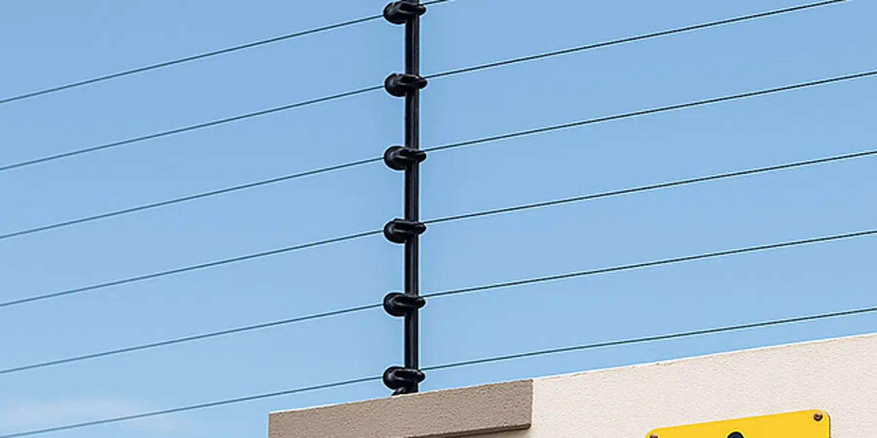 Cerco eléctrico instalado sobre el muro de una casa, con cartel de advertencia
