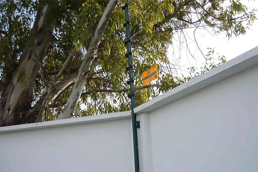 Cerco eléctrico sobre la medianera de una casa con árboles